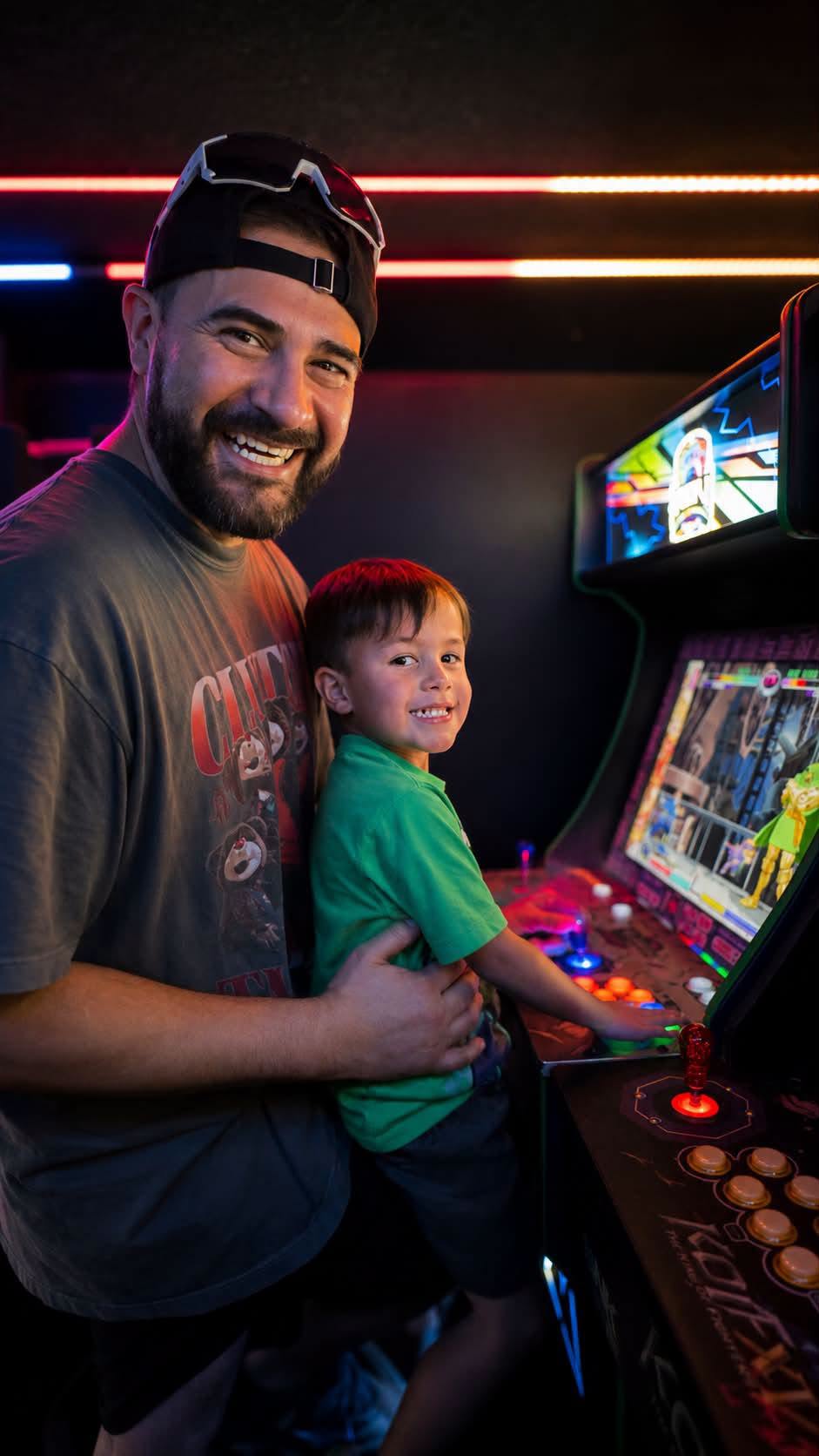 A father and son playing a lit custom arcade cabinet inside the RGV Games on Wheelz bus