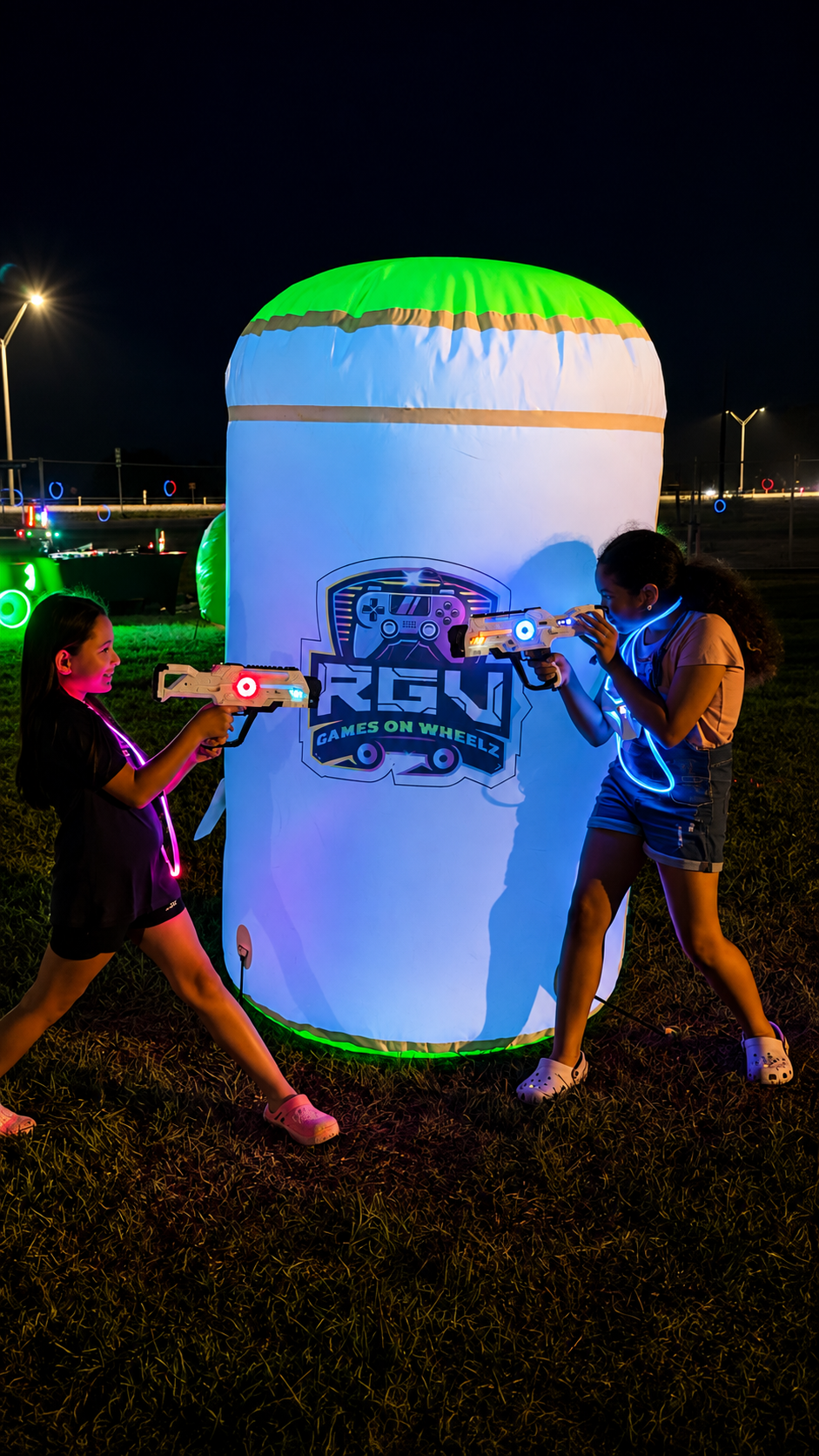 Two young players taking cover behind a glowing inflatable bunker during a night mobile laser tag game
