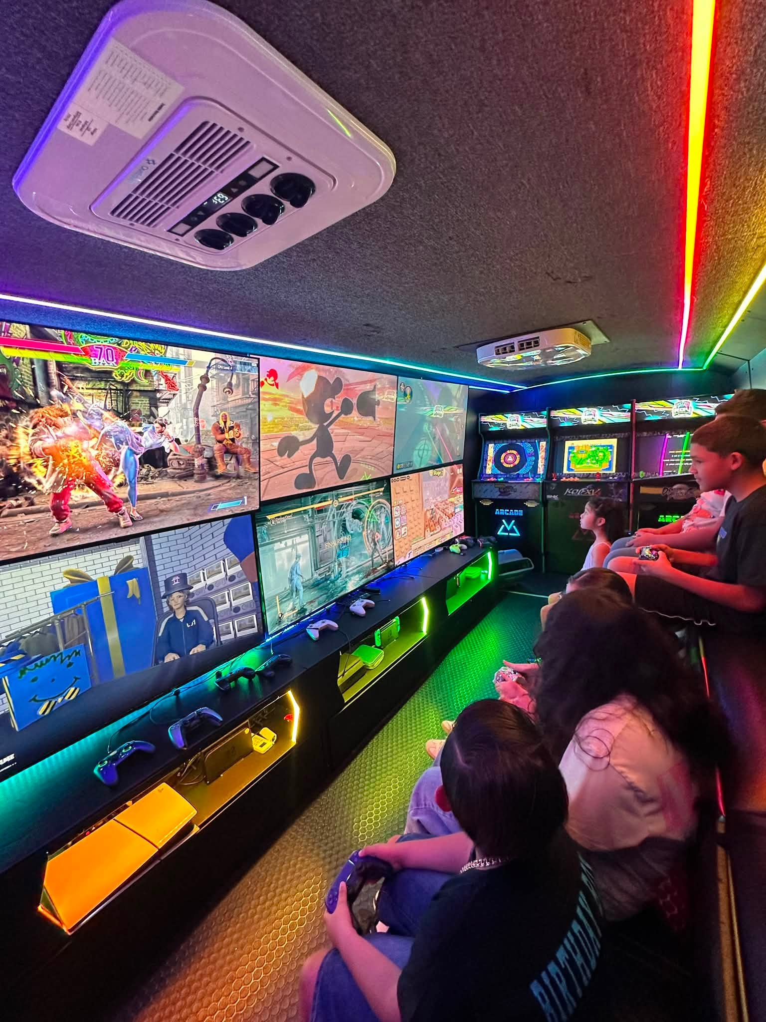 Guests playing at the gaming stations inside the RGV Games on Wheelz bus with the screen wall lit up