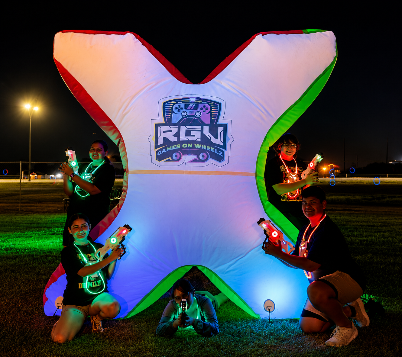 Players in light-up vests taking cover behind a glowing inflatable barrier during an RGV Games on Wheelz mobile laser tag game at night